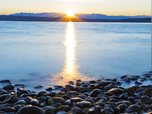 Photo of rocky Puget Sound shoreline with the sun rising over the water